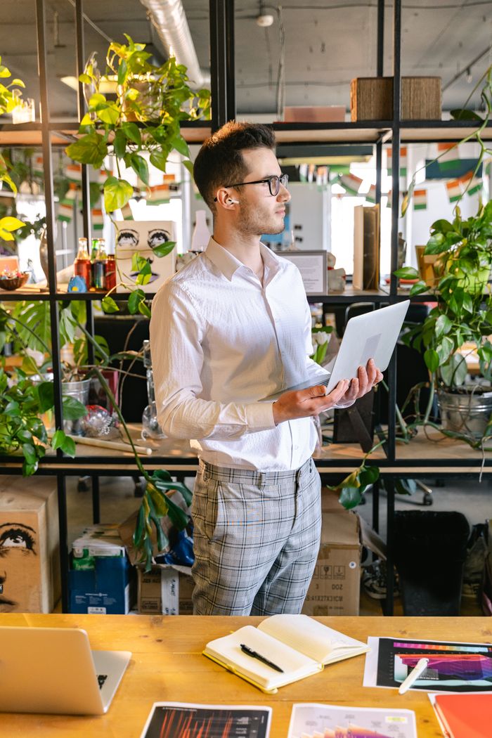Caucasian man in corporate attire working on laptop in an indoor office with plants.